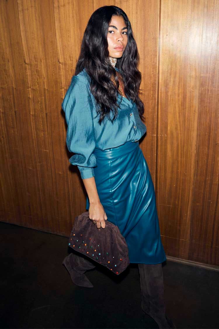Teal Vegan Leather Jaspre Skirt styled with a matching teal shirt and a brown studded clutch.