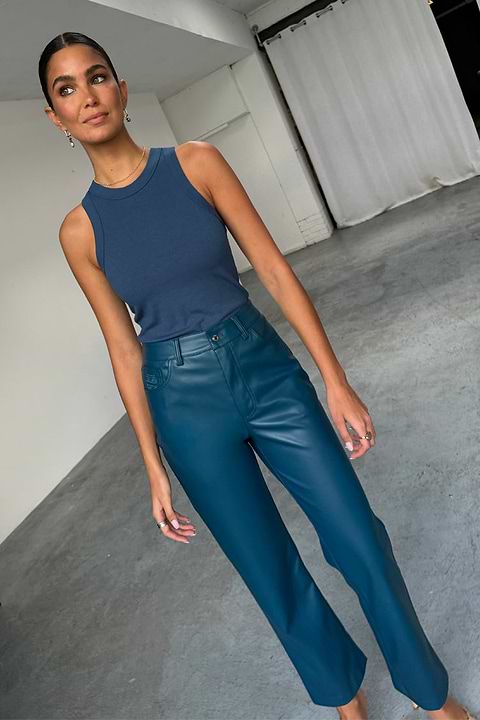 Teal straight leg vegan leather trousers and a navy ribbed tank top worn by a model.