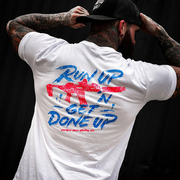 A man holding his black hat in a white Combat Iron Apparel t-shirt.