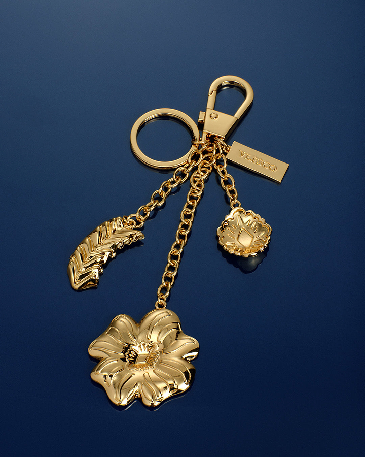 Gold keychain with floral and leaf designs on a blue background