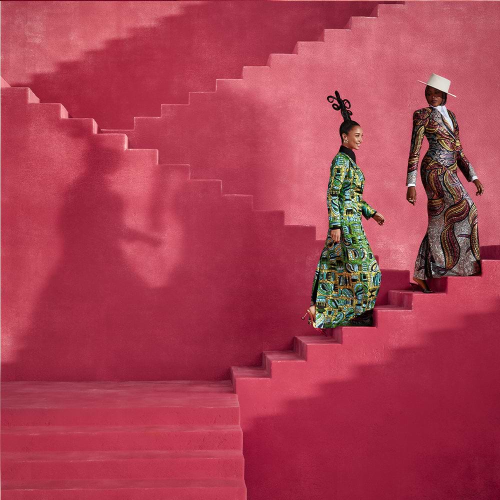 Two women in printed dress climbing red stairs