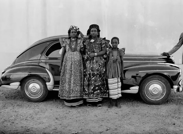 Black and white photo of two women and a boy in front of a car