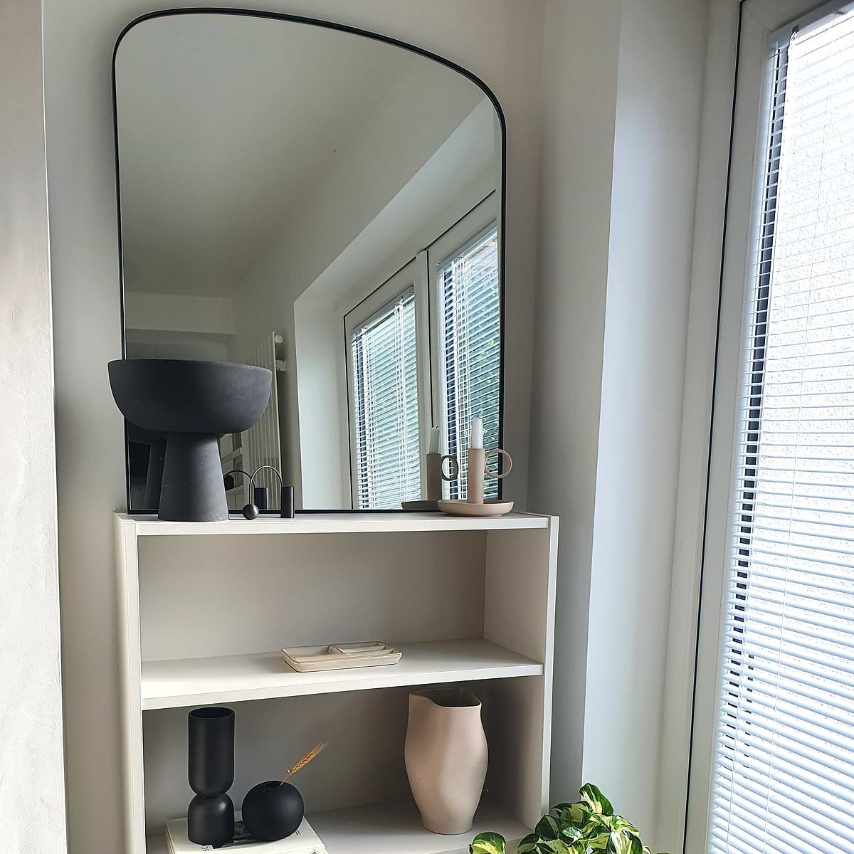 Black contemporary arched metal wall mirror displayed beside window