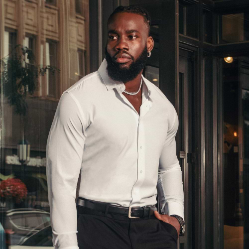 Man in a white shirt and black pants standing in front of a building entrance.