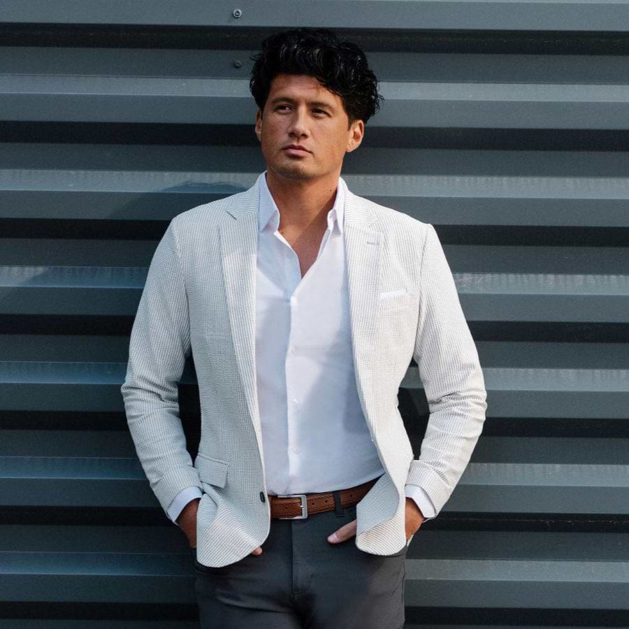 Man in a light gray blazer and white shirt standing against a corrugated metal wall.
