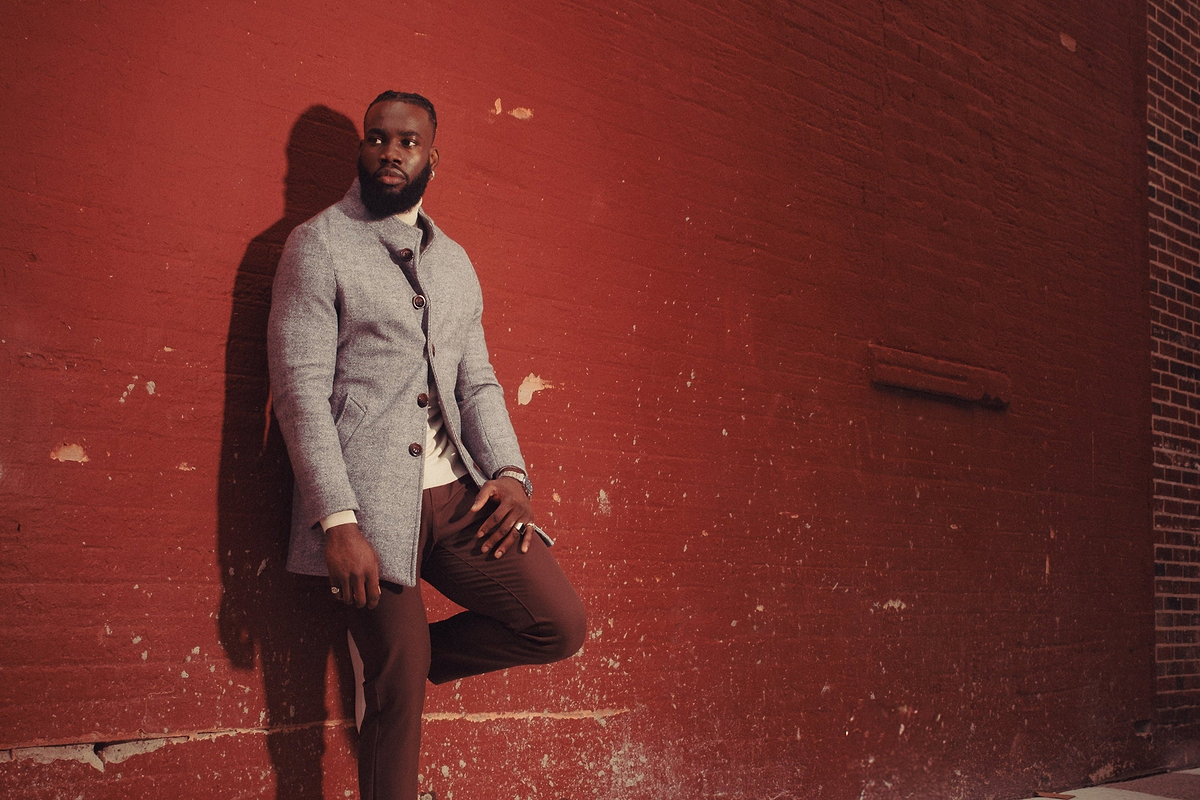 Man in a gray coat standing against a red brick wall