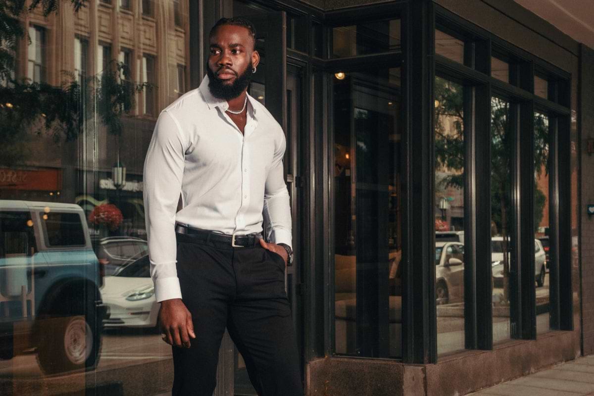 Man in a white shirt and black pants standing in front of a glass building entrance.
