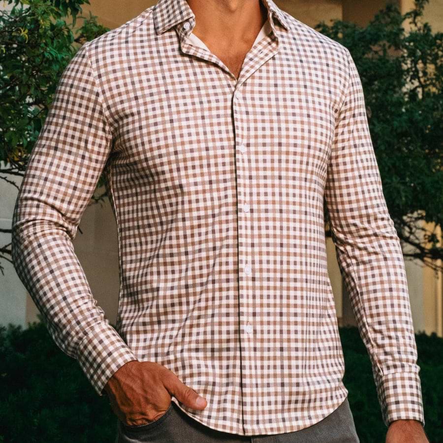 Man wearing a checkered shirt outdoors with greenery in the background
