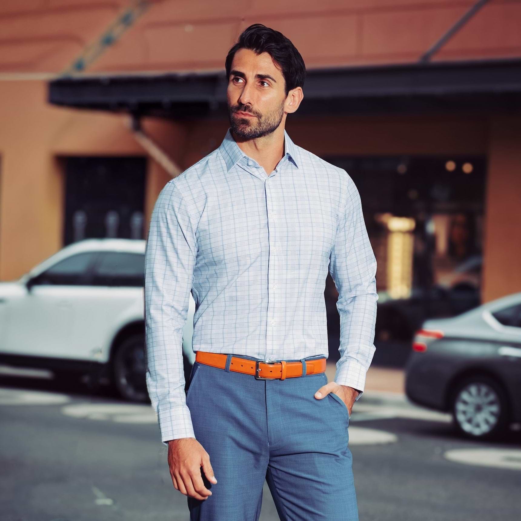 Man in a light blue checkered shirt and blue pants standing on a street.