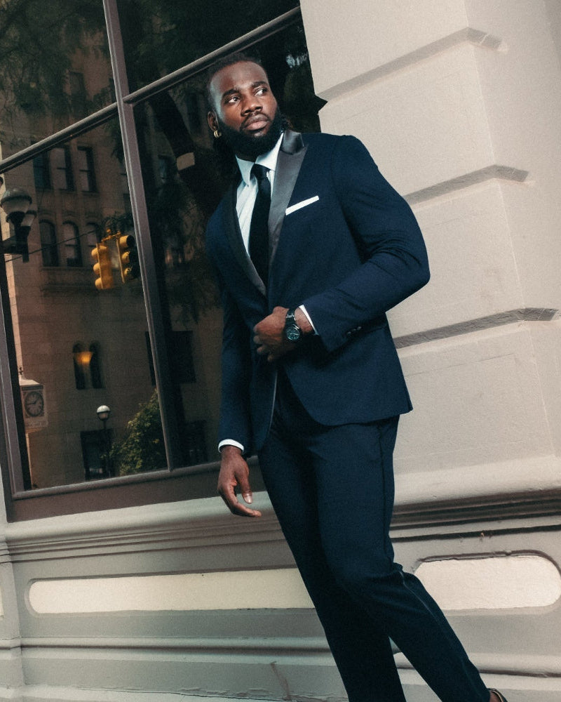 Man in a navy suit standing in front of a building with large windows.