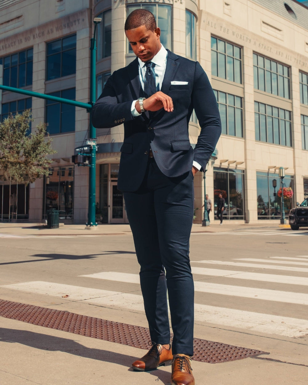 Man in a navy suit standing on a city street corner.