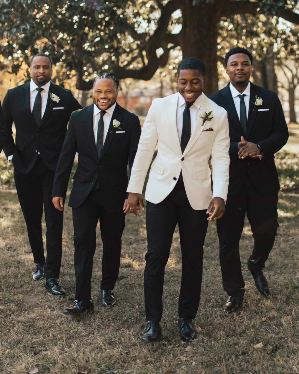 Four men in formal attire standing outdoors with trees in the background