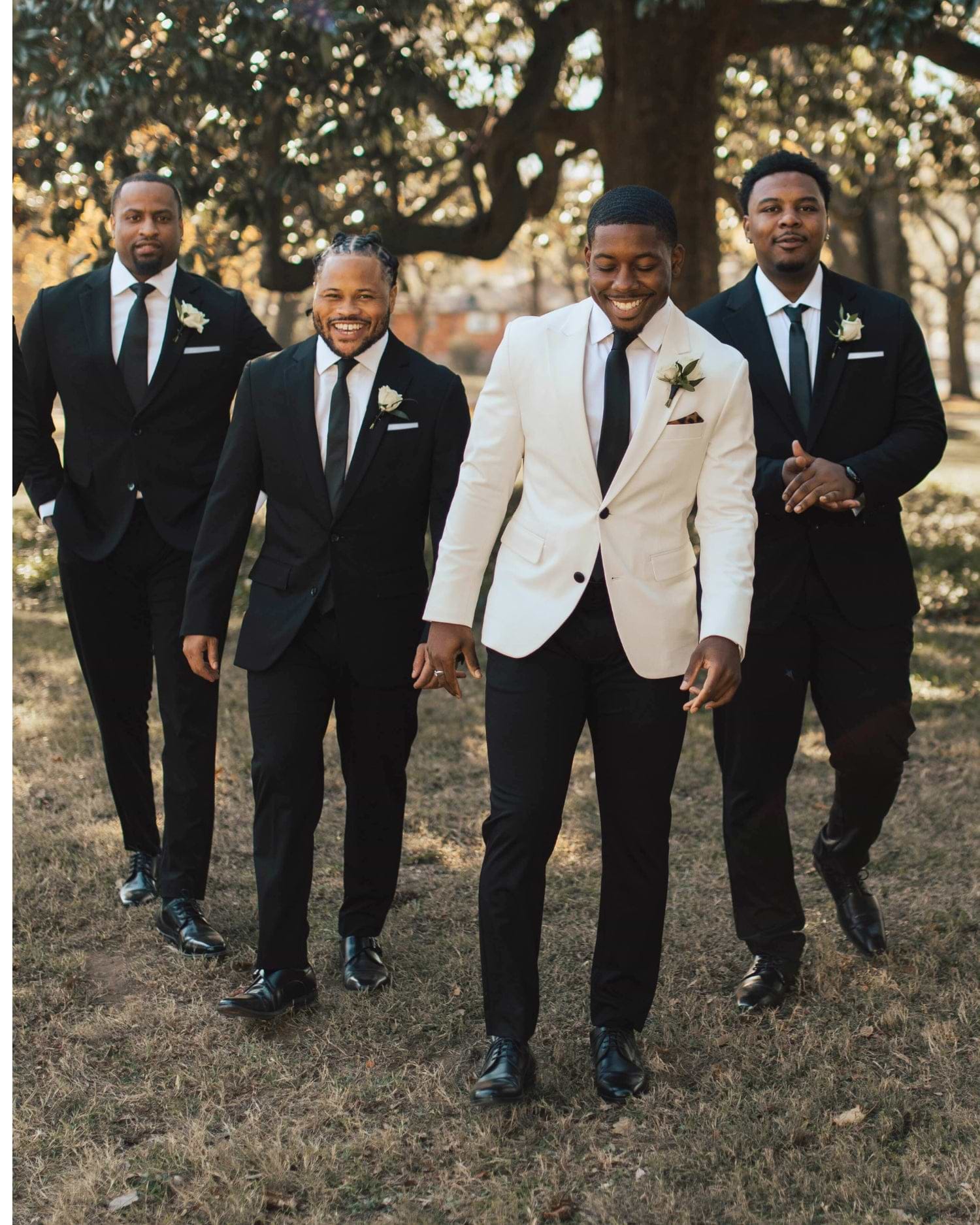 Four men in formal attire standing outdoors with trees in the background