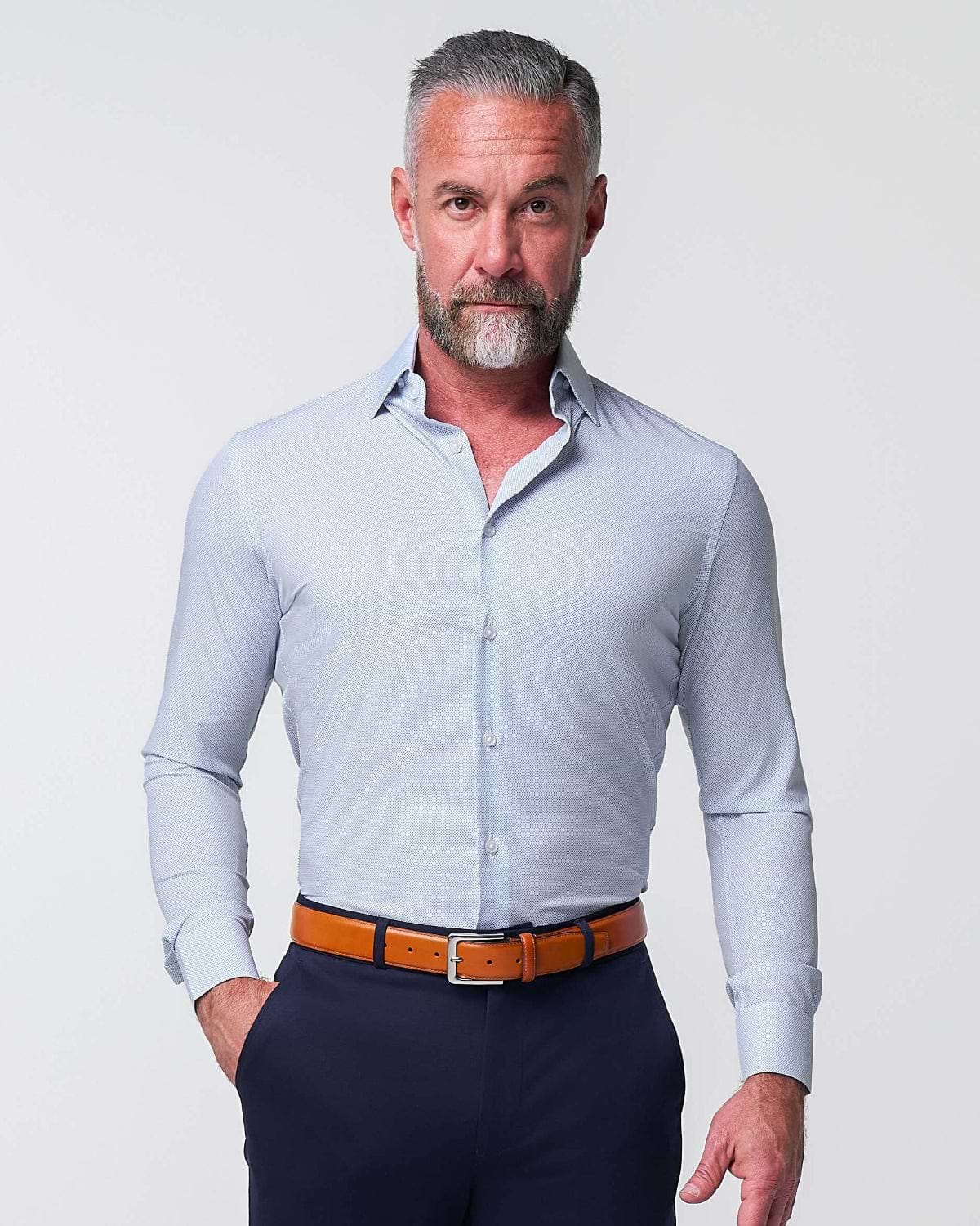 Man wearing a light blue dress shirt, navy pants, and brown shoes on a white background