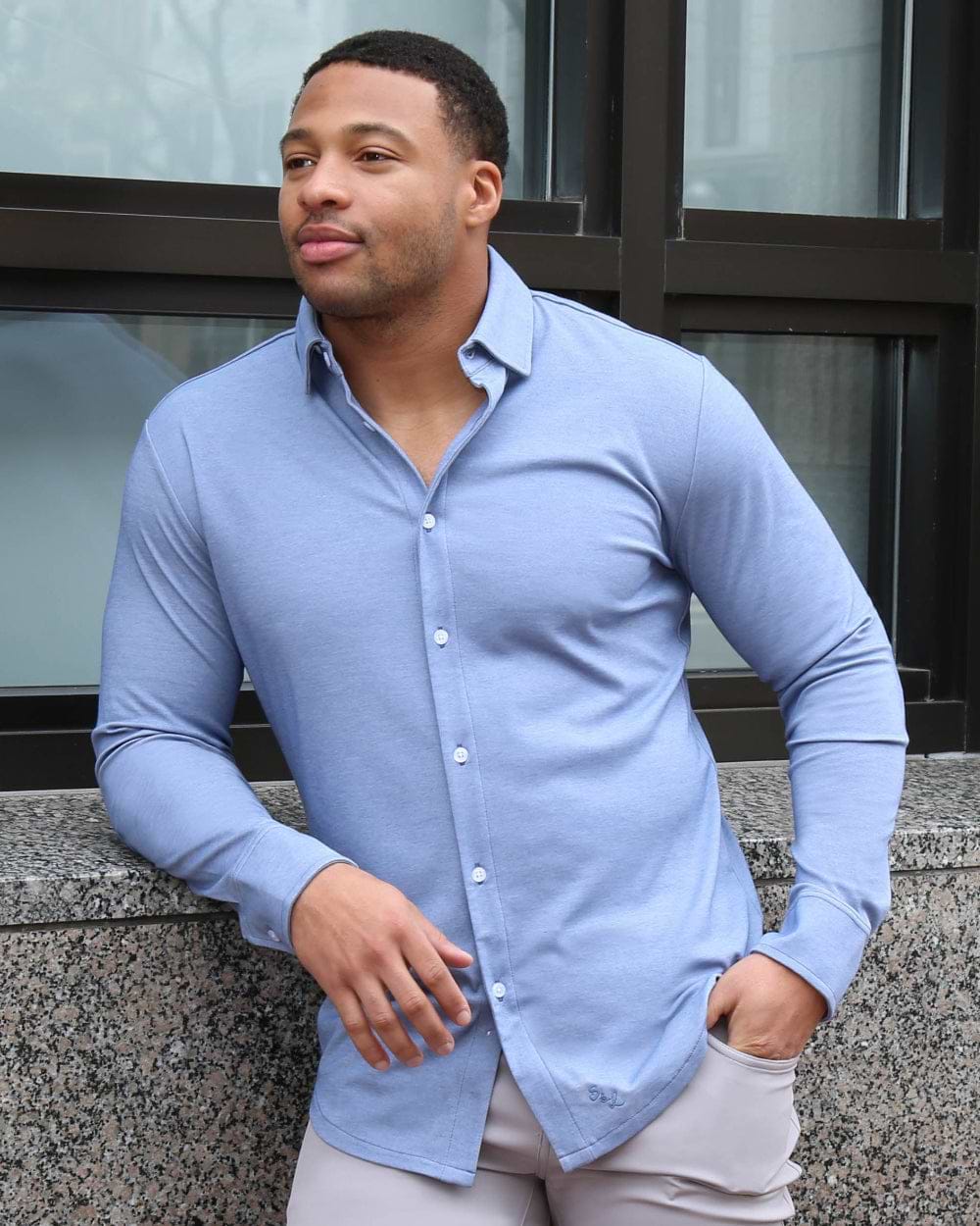 Man wearing a light blue button-up shirt leaning against a building.