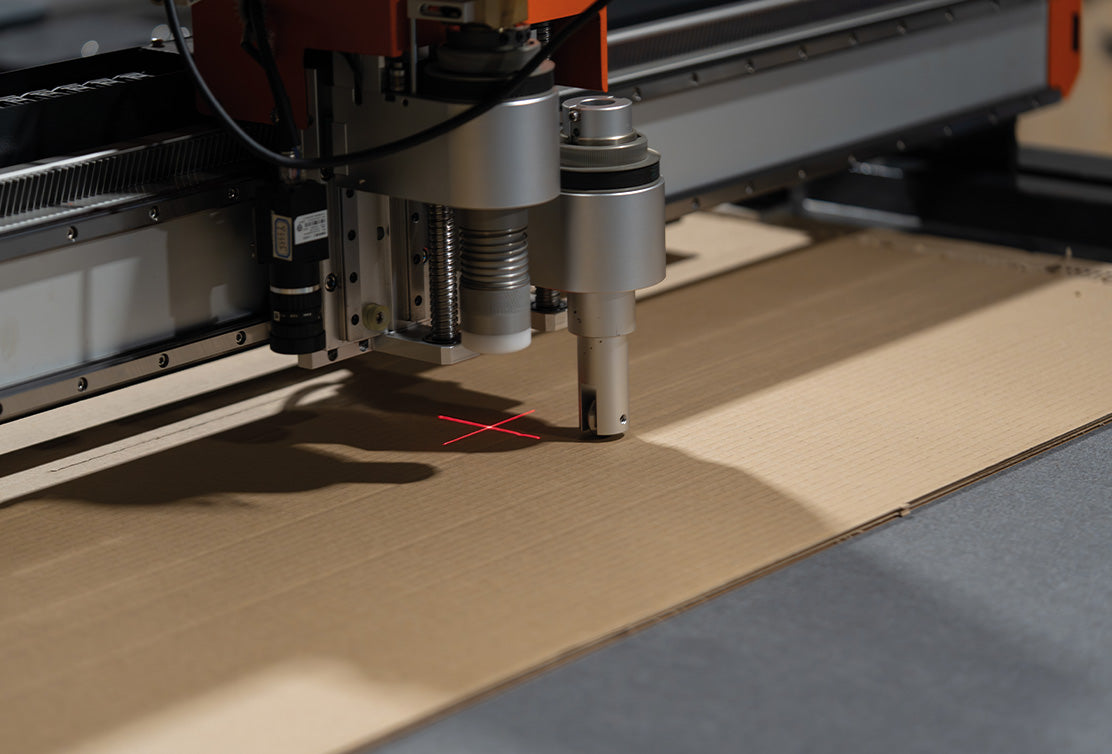 Laser machinery altering a sheet of cardboard.