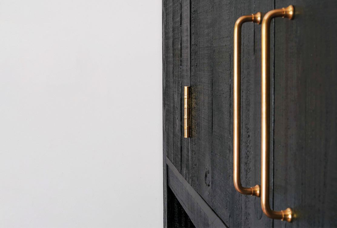 Close-up of a brass door handle on a textured black wooden surface, showcasing a sleek and modern design.