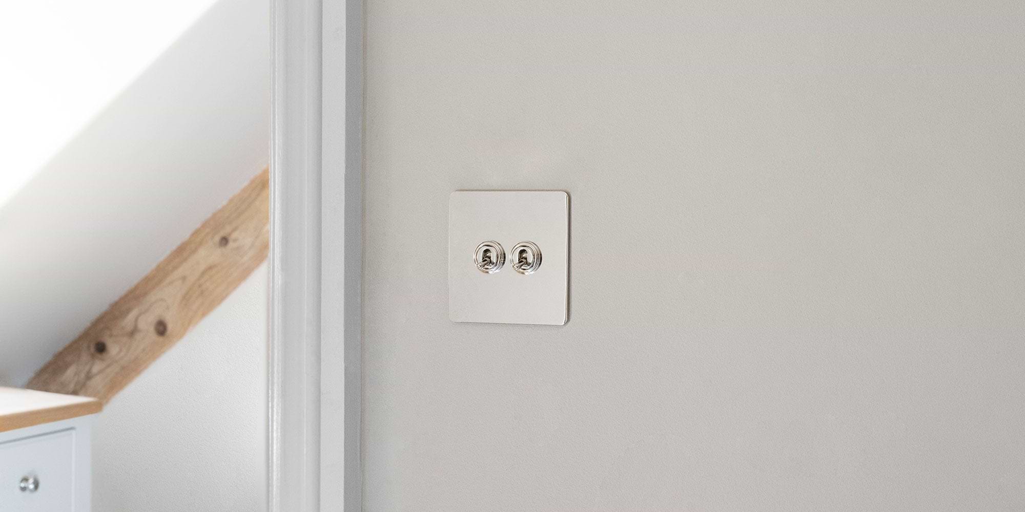 A stylish light switch and dual socket set featuring a sleek chrome finish on a floral patterned wall.