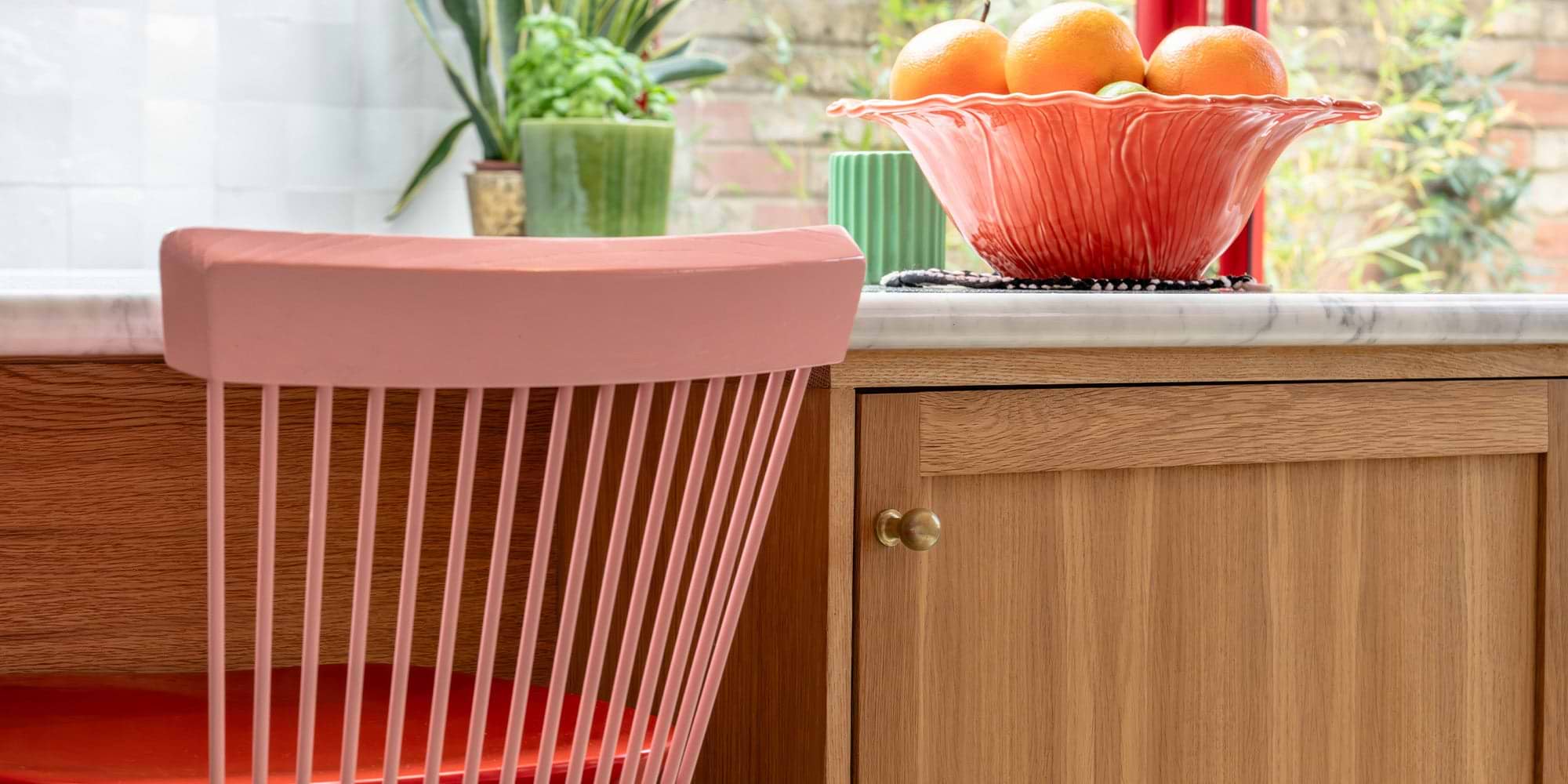 Modern kitchen cabinet with brass handles and colorful chairs in the foreground.