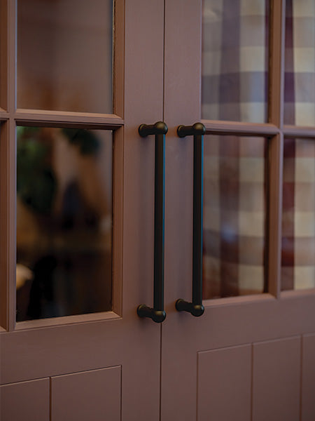 Close-up of stylish cabinet doors with black metal handles and glass panels, featuring a checkered fabric backdrop.