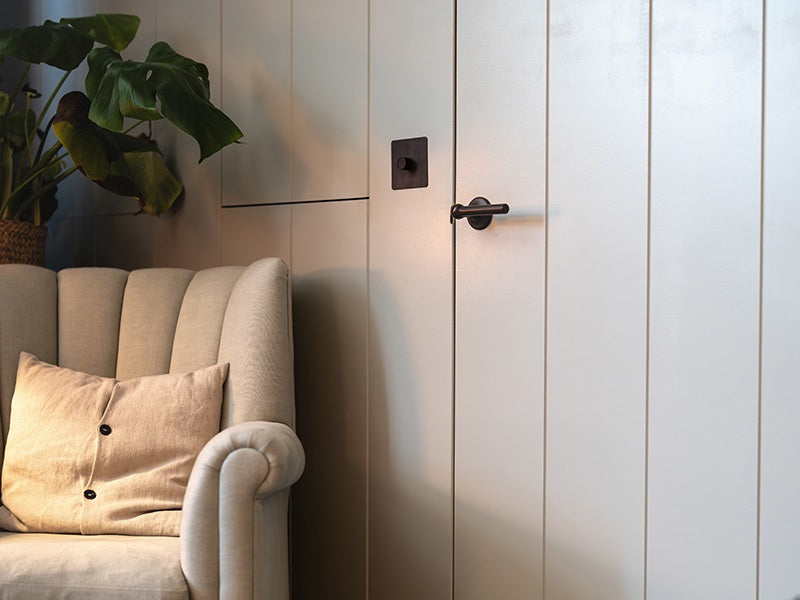 A cozy room features a light-colored, tufted sofa, a decorative pillow, and a sleek door with minimalistic black hardware.