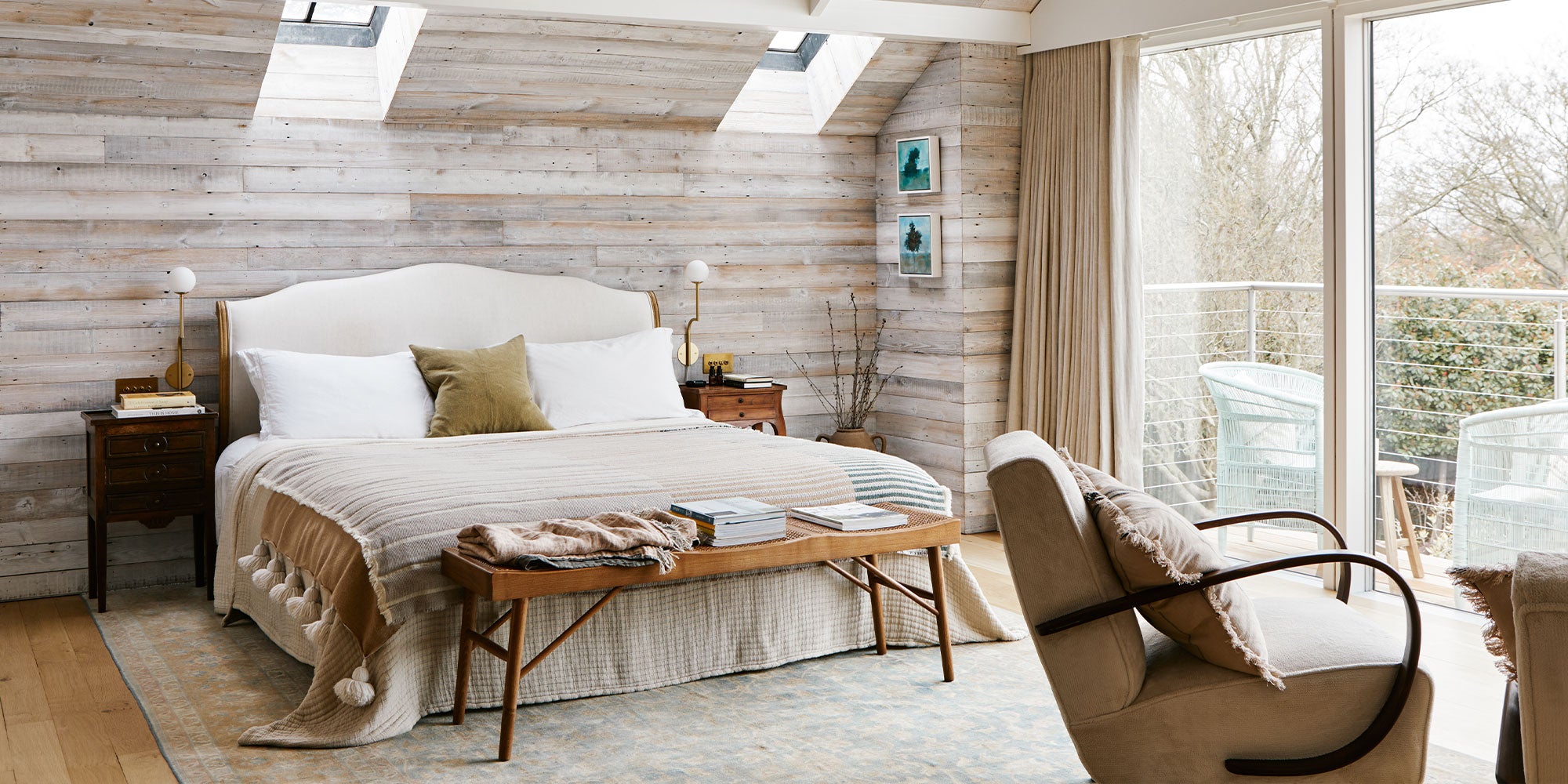 Cozy bedroom featuring a king-sized bed, wooden accent wall, and natural light from skylights, with a chair and balcony view.