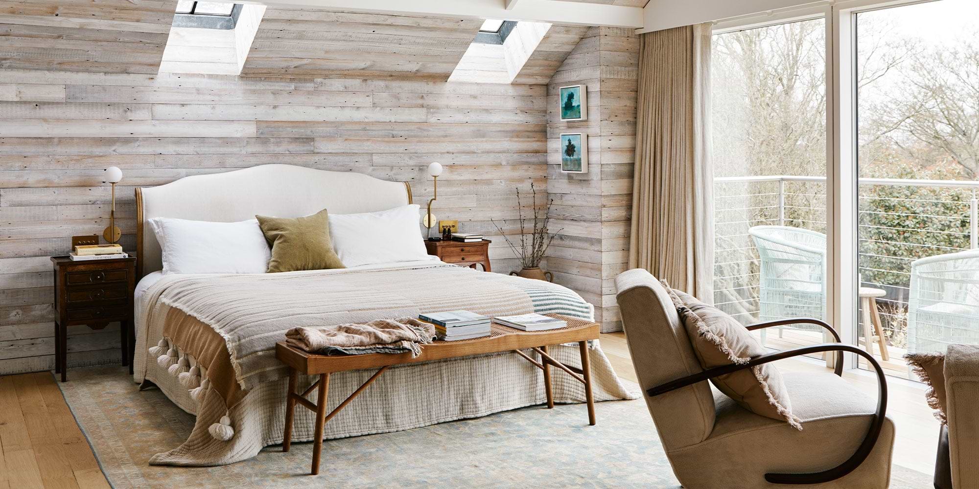 Cozy bedroom featuring a king-sized bed, wooden accent wall, and natural light from skylights, with a chair and balcony view.