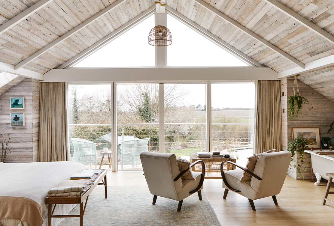 Cozy, lightly decorated room with wood-panelled walls, large windows, and two armchairs overlooking a serene outdoor view.