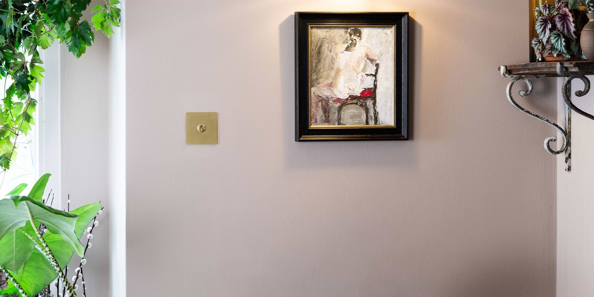 A wall adorned with a framed painting of a seated figure, complemented by a wall-mounted shelf and vibrant green plants nearby.