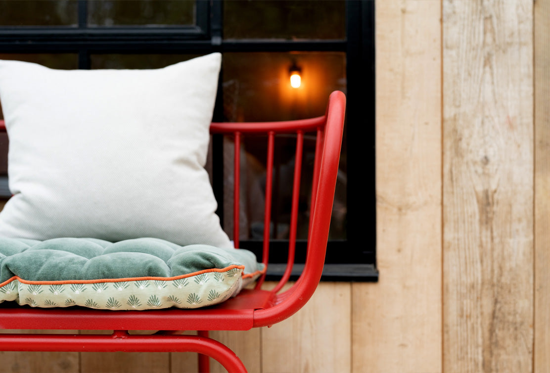 A cozy red chair with a plush green cushion and white pillow, set against wooden walls and a softly lit window.