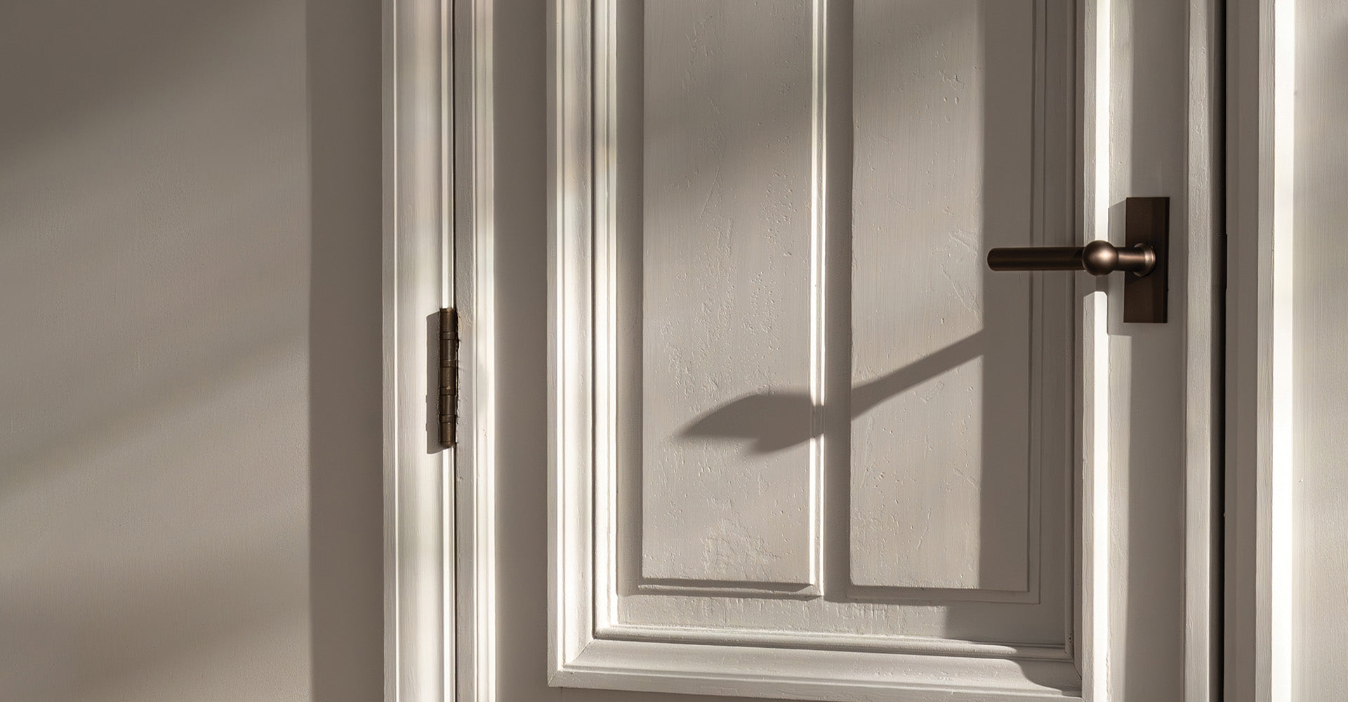 Close-up of a white door with a bronze handle, casting soft shadows from natural light on a textured surface.