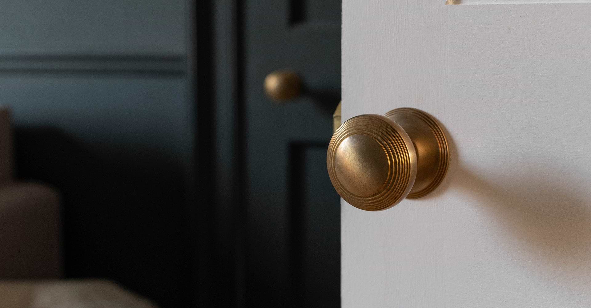 Close-up of a stylish brass door knob on a white wall, with a blurred black door in the background.