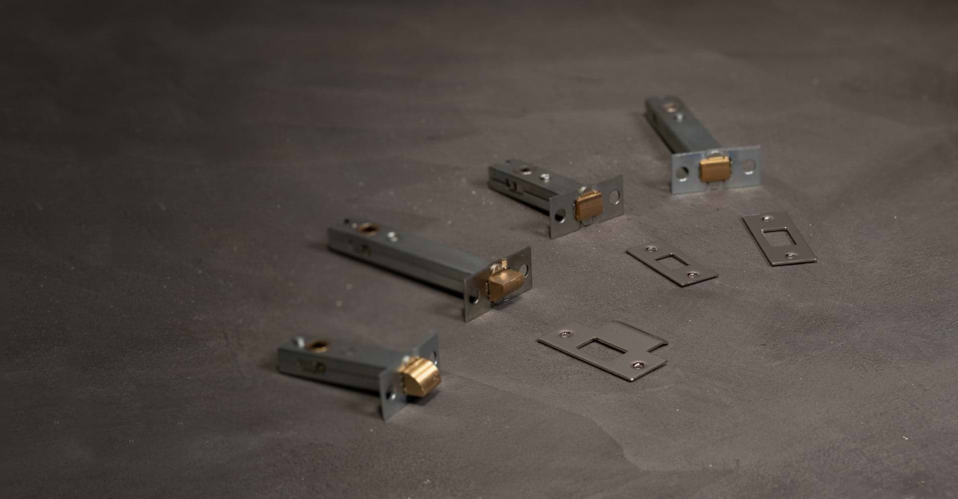 Collection of metal slide bolts and strike plates arranged on a dark surface, showcasing various lock hardware components.