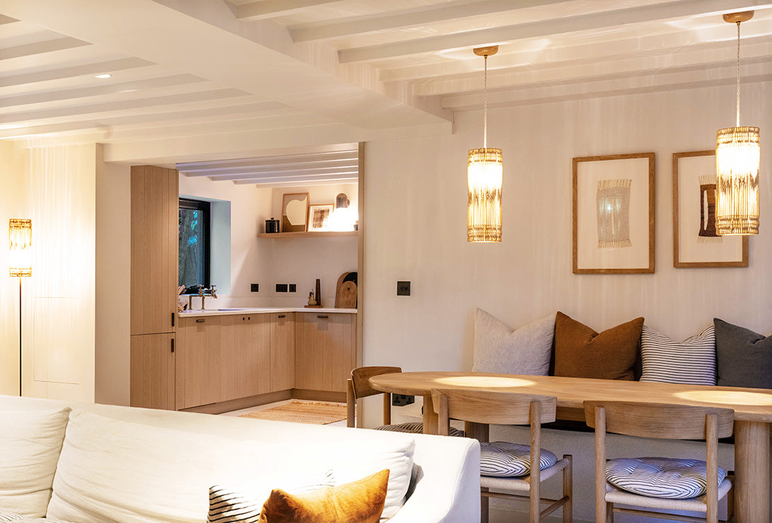 Cozy living space featuring a modern kitchen, wooden dining table, elegant lighting, and decorative cushions in warm tones.