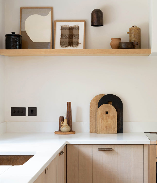 A modern kitchen shelf with art, decorative vases, and wooden cutting boards, featuring minimalist design elements in neutral tones.