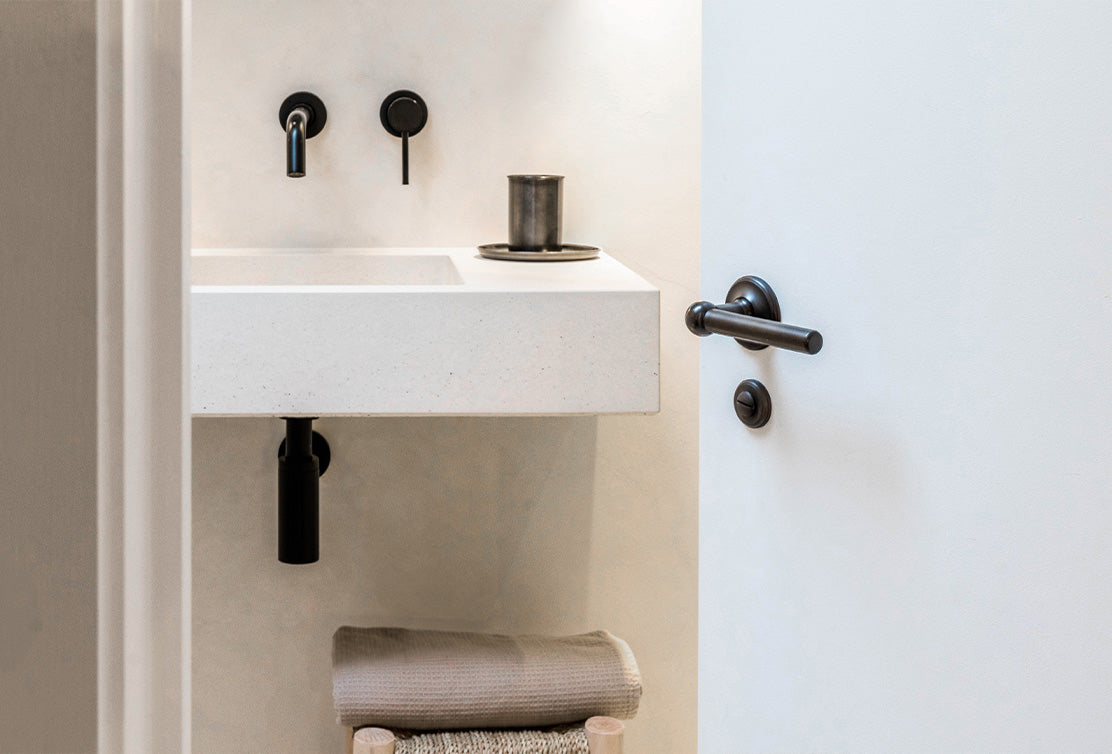 Modern bathroom featuring a minimalist white sink, black fixtures, and neatly folded towels on a wooden rack.