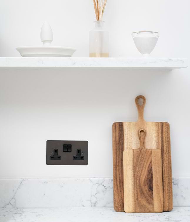 A wooden cutting board set leans against a white wall, next to a black power outlet and a minimalist kitchen shelf décor.