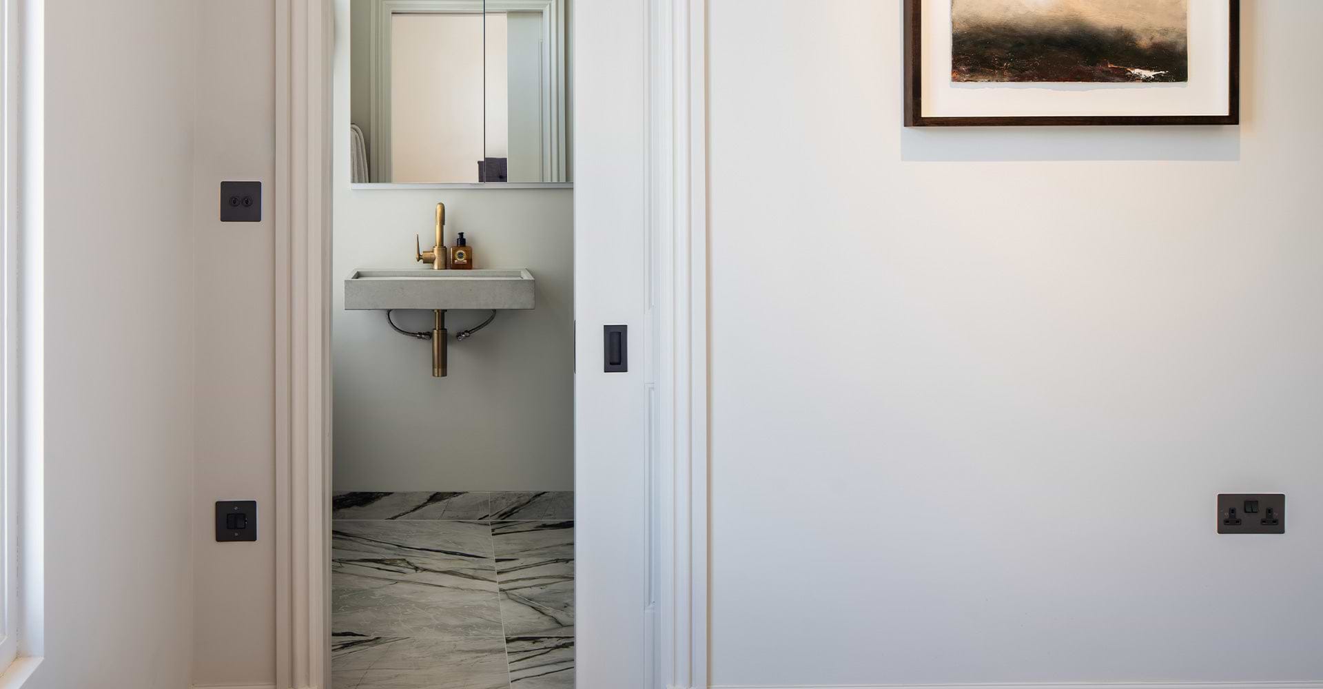 A modern bathroom view featuring a sleek concrete sink, gold faucet, and marble floor, framed by stylish black door switches.