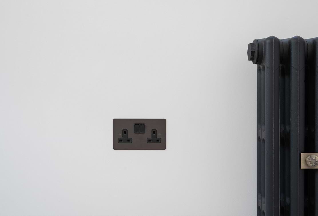 A black electrical outlet with a switch mounted on a white wall next to a stylish black radiator.
