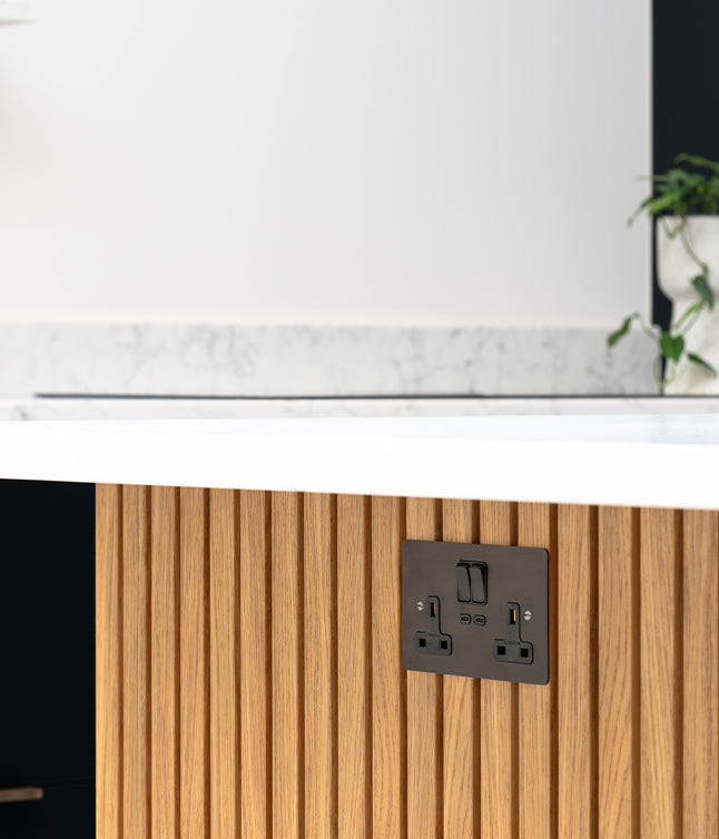 A modern kitchen with a wooden panel, featuring a stylish black power outlet against a white marble countertop backdrop.