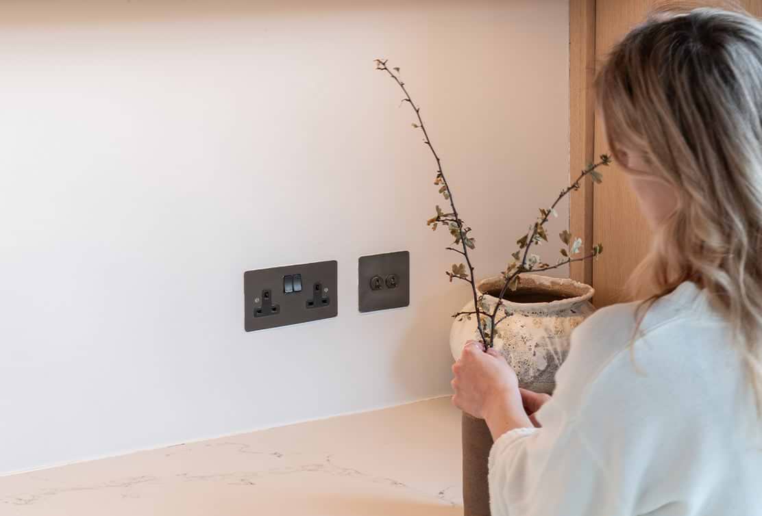 Person arranging a dried plant, besides some bronze light switches
