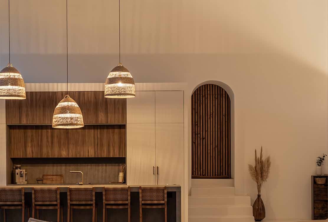 Modern kitchen with woven pendant lights, wooden cabinetry, and a staircase with a wooden arched entrance to the right.