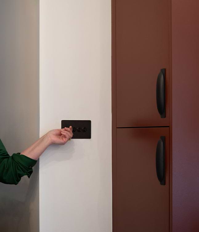 A person's hand adjusts a sleek black light switch next to a modern brown cabinet in a minimalist kitchen setting.