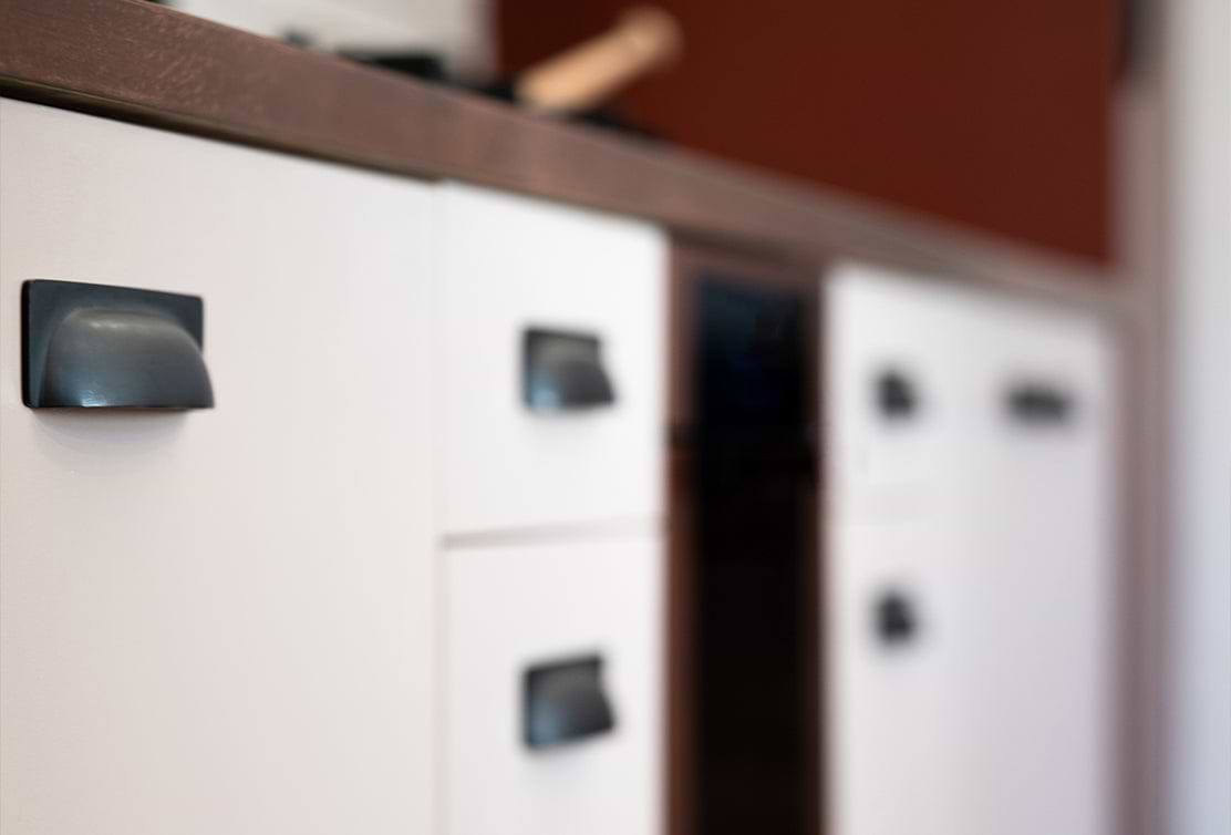 Close-up of white kitchen cabinets with black handles, wooden countertop, and a blurred background.