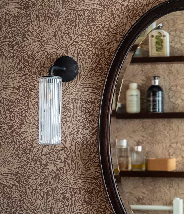 A stylish bathroom featuring floral wallpaper, a round mirror, a glass light fixture, and a minimalist sink with shelving.