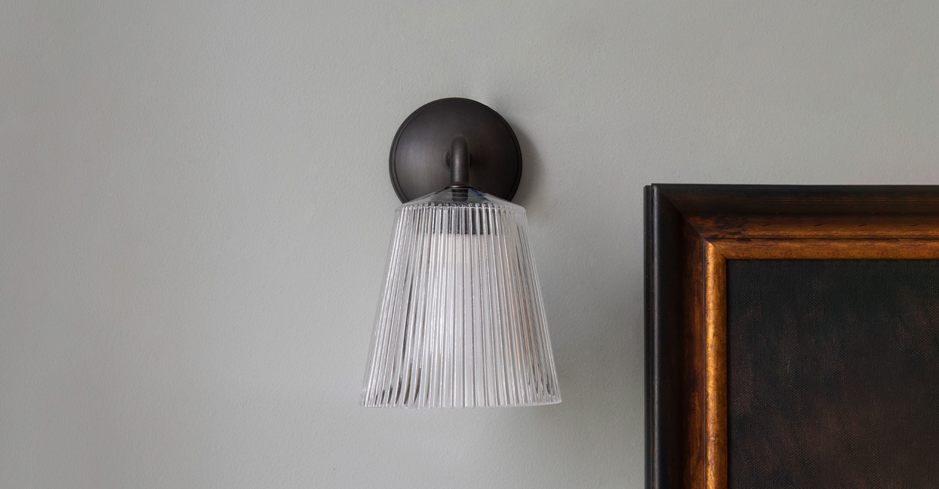 A modern wall sconce with a fluted glass shade illuminates a neutral wall, accompanied by framing elements, conveying a stylish ambiance.