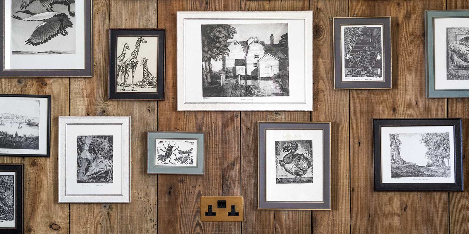 A collage of black-and-white animal and landscape prints framed against a rustic wooden wall, showcasing diverse artistic styles.