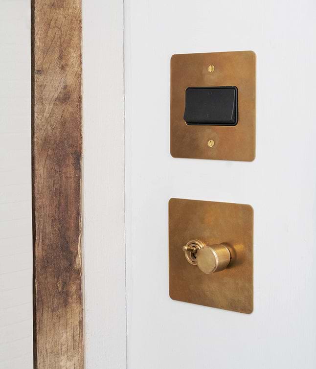 Close-up of a white door with a brass light switch and a round brass door lock, adjacent to natural wood trim.