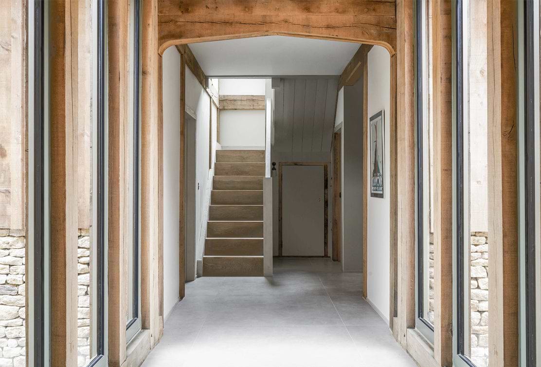 Bright hallway featuring wooden accents, large windows, and a staircase leading to the upper floor, creating a modern rustic aesthetic.