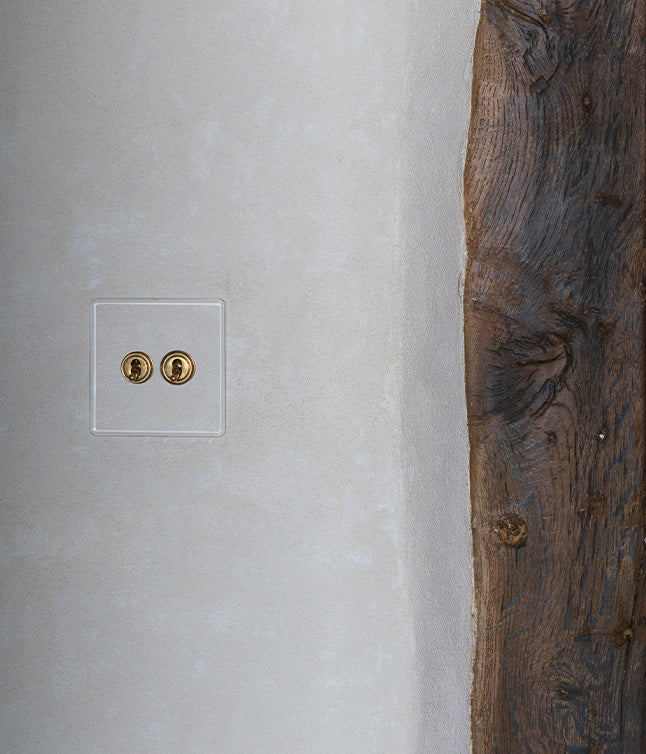 A close-up of a modern light switch with brass fixtures on a smooth beige wall, next to a rough, textured wooden panel.